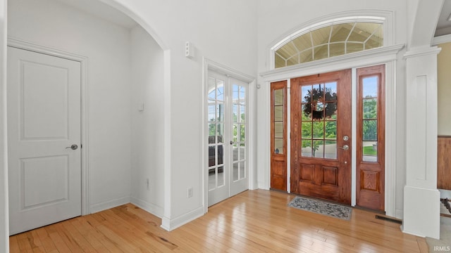 foyer with light wood-style flooring, visible vents, arched walkways, and baseboards