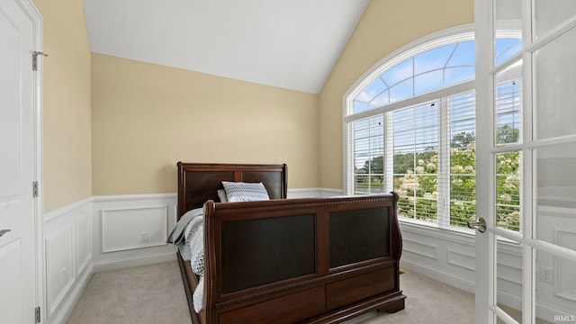 bedroom featuring light carpet, vaulted ceiling, a decorative wall, and multiple windows