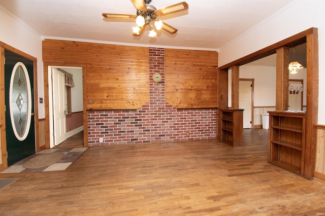 interior space with ornamental molding, ceiling fan, wood walls, and wood finished floors