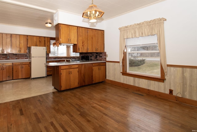 kitchen featuring wainscoting, dark wood-style floors, brown cabinets, freestanding refrigerator, and a chandelier