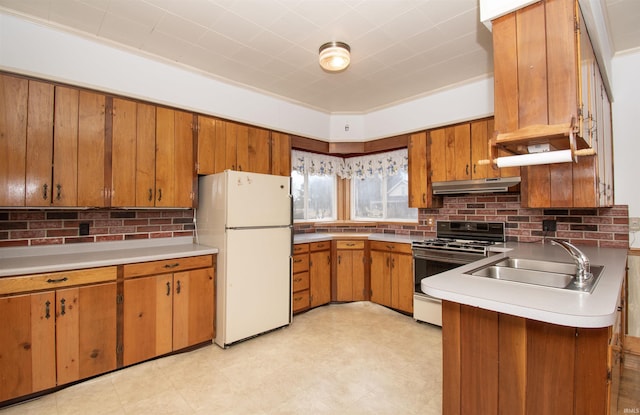 kitchen with under cabinet range hood, gas range oven, a sink, freestanding refrigerator, and brown cabinetry