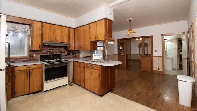 kitchen featuring a wainscoted wall, gas range oven, brown cabinetry, and under cabinet range hood