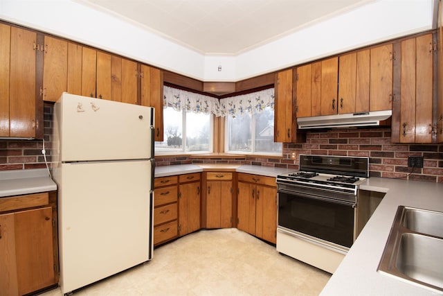 kitchen with brown cabinetry, freestanding refrigerator, gas stove, a sink, and under cabinet range hood