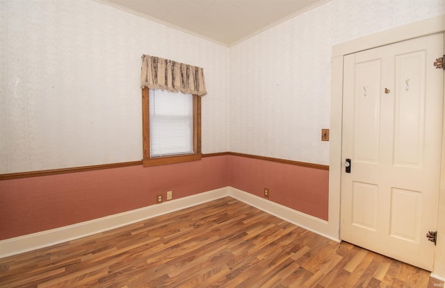 empty room with crown molding, baseboards, wood finished floors, and wallpapered walls