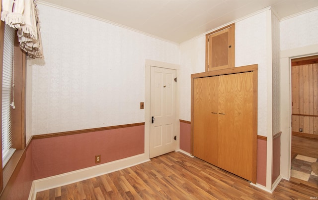 unfurnished bedroom featuring wallpapered walls, baseboards, ornamental molding, and wood finished floors