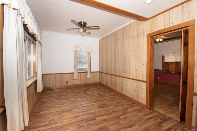 spare room with a wainscoted wall, ornamental molding, ceiling fan, wood walls, and wood finished floors