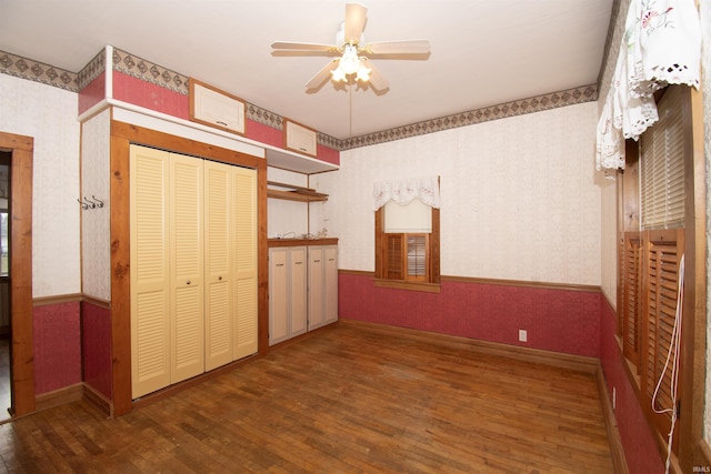 unfurnished bedroom featuring wallpapered walls, baseboards, hardwood / wood-style floors, and a wainscoted wall