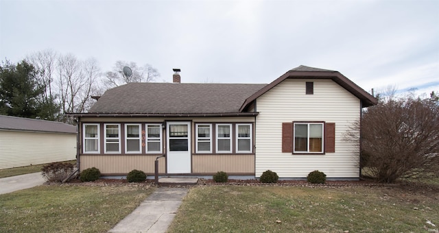 view of front of property with a shingled roof, a chimney, and a front lawn