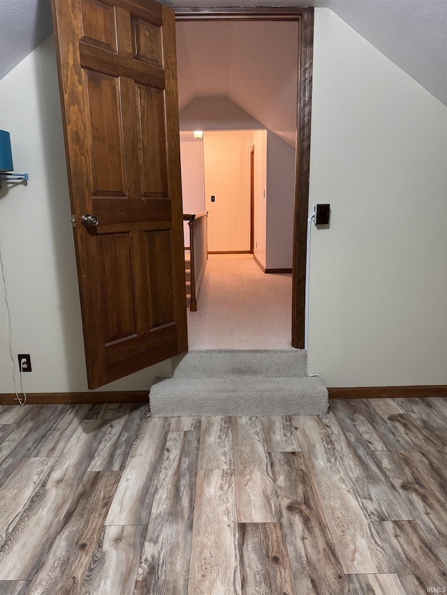 hallway featuring baseboards, vaulted ceiling, and wood finished floors