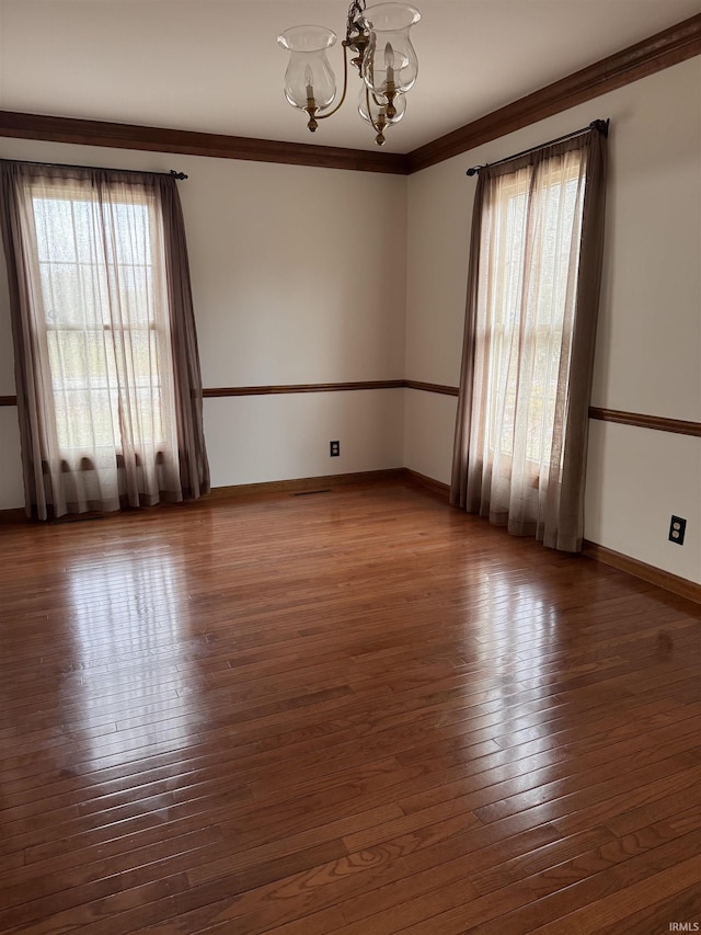 unfurnished room with crown molding, wood-type flooring, baseboards, and a notable chandelier