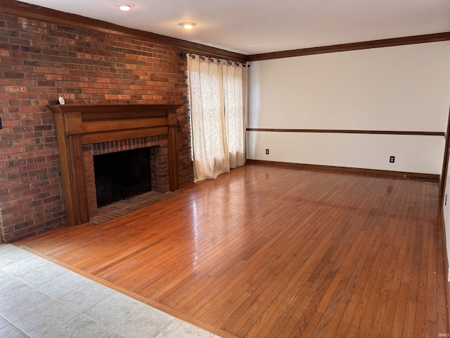 unfurnished living room with a brick fireplace, crown molding, wood-type flooring, and baseboards