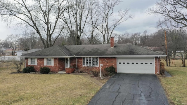 ranch-style house featuring driveway, brick siding, a chimney, an attached garage, and a front yard