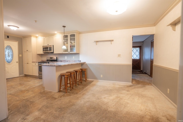 kitchen with a wainscoted wall, a breakfast bar, appliances with stainless steel finishes, glass insert cabinets, and crown molding