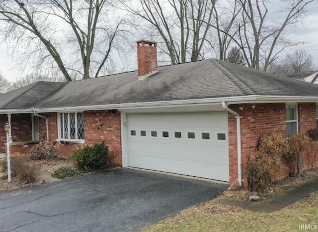 view of side of home with a garage, a shingled roof, a chimney, aphalt driveway, and brick siding