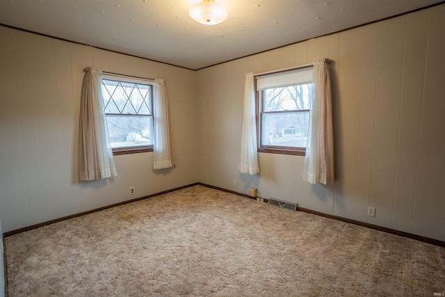 carpeted spare room with a healthy amount of sunlight, baseboards, and visible vents