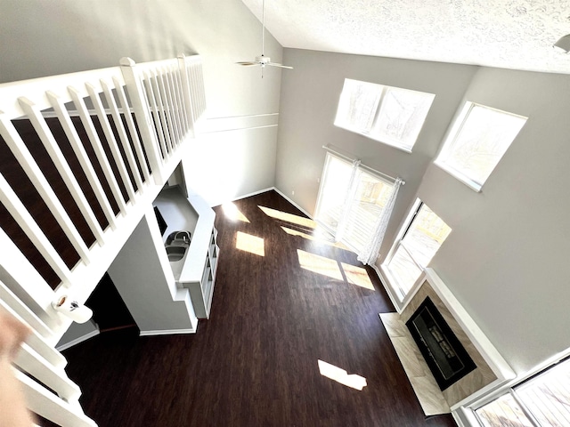 unfurnished living room with a tiled fireplace, a ceiling fan, a textured ceiling, wood finished floors, and high vaulted ceiling