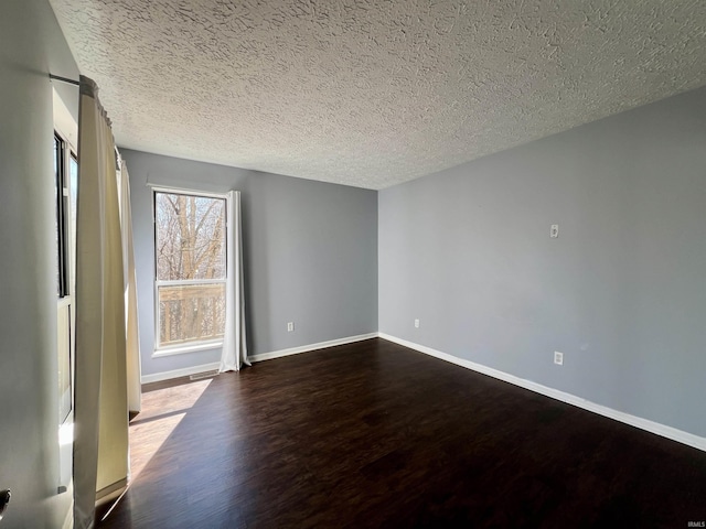 spare room featuring baseboards, dark wood finished floors, and a textured ceiling