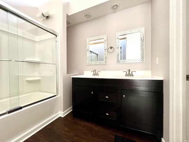 full bathroom featuring shower / bath combination with glass door, a sink, wood finished floors, baseboards, and double vanity