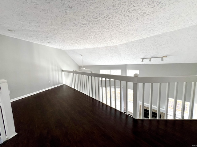 unfurnished room featuring lofted ceiling, a textured ceiling, wood finished floors, baseboards, and rail lighting