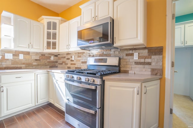 kitchen featuring white cabinetry, light countertops, appliances with stainless steel finishes, decorative backsplash, and glass insert cabinets