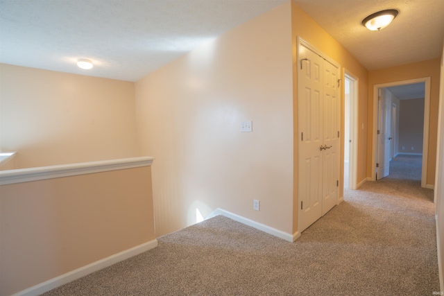 hallway with carpet floors, baseboards, a textured ceiling, and an upstairs landing