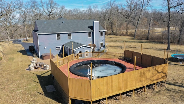 rear view of house featuring roof with shingles, a yard, a chimney, a hot tub, and fence