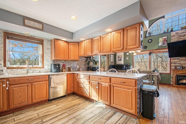 kitchen with a warm lit fireplace, a peninsula, light countertops, stainless steel dishwasher, and a sink