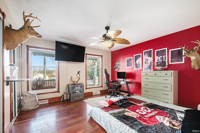 bedroom featuring wood-type flooring, visible vents, an accent wall, ceiling fan, and baseboards