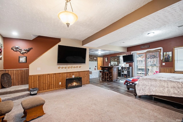 bedroom with a textured ceiling, wood walls, wainscoting, and a glass covered fireplace