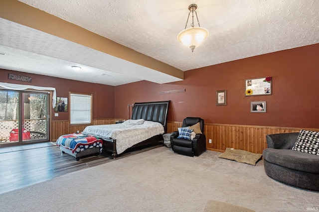 bedroom with access to outside, a textured ceiling, and wainscoting