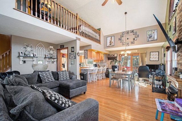 living room with light wood-style floors, a high ceiling, and ceiling fan with notable chandelier