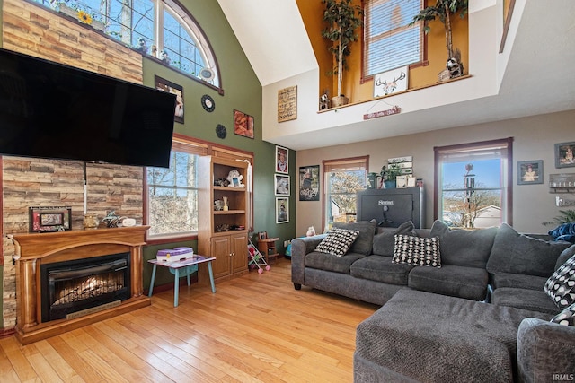 living area featuring a warm lit fireplace, high vaulted ceiling, a wealth of natural light, and hardwood / wood-style flooring