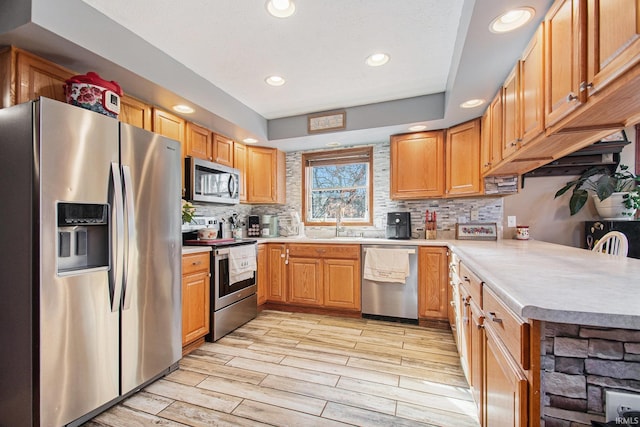 kitchen with light wood finished floors, tasteful backsplash, appliances with stainless steel finishes, light countertops, and recessed lighting