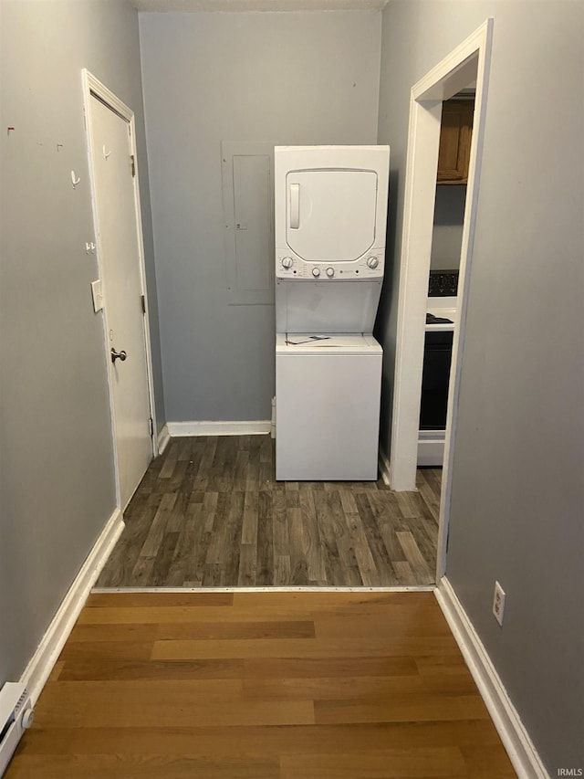 laundry room featuring a baseboard radiator, baseboards, stacked washer / dryer, and wood finished floors