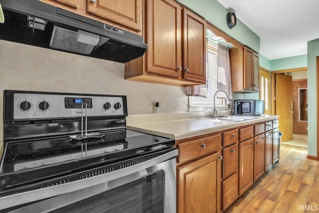 kitchen with light wood finished floors, light countertops, electric range, a sink, and exhaust hood