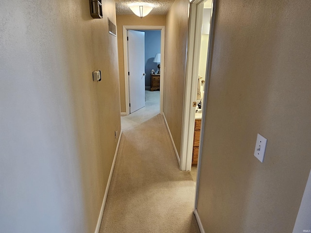 hallway featuring light carpet, baseboards, visible vents, and a textured ceiling