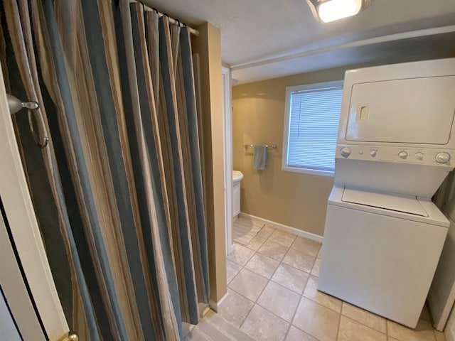 washroom with laundry area, light tile patterned flooring, stacked washer and clothes dryer, and baseboards