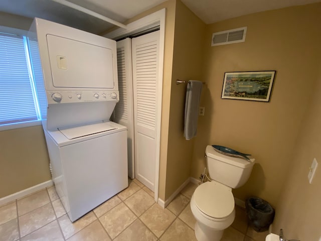 bathroom featuring visible vents, toilet, stacked washing maching and dryer, tile patterned flooring, and baseboards