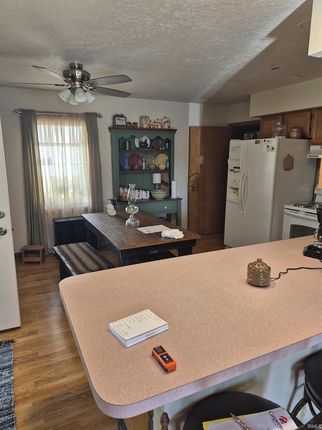 kitchen with a breakfast bar area, light countertops, a textured ceiling, wood finished floors, and white appliances