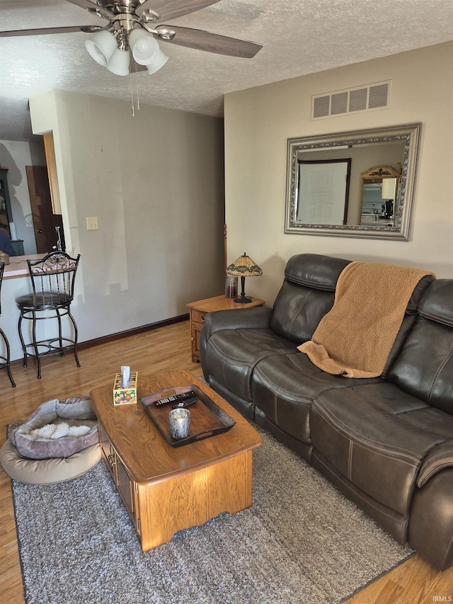 living area featuring visible vents, a ceiling fan, a textured ceiling, wood finished floors, and baseboards