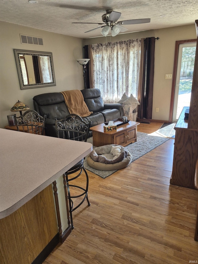 living area featuring visible vents, ceiling fan, a textured ceiling, and wood finished floors