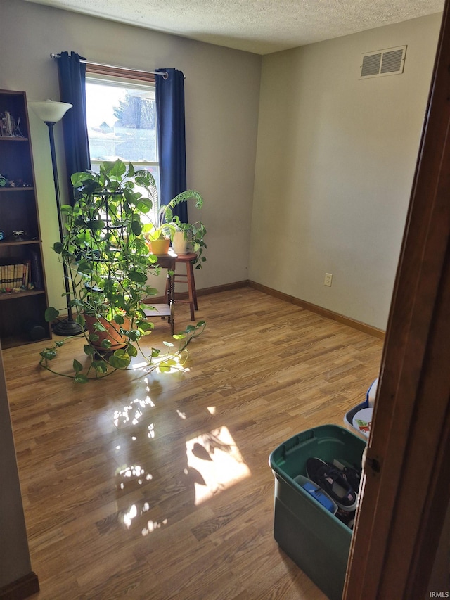 empty room with visible vents, a textured ceiling, baseboards, and wood finished floors