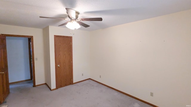 unfurnished bedroom with light carpet, baseboards, ceiling fan, a textured ceiling, and a closet