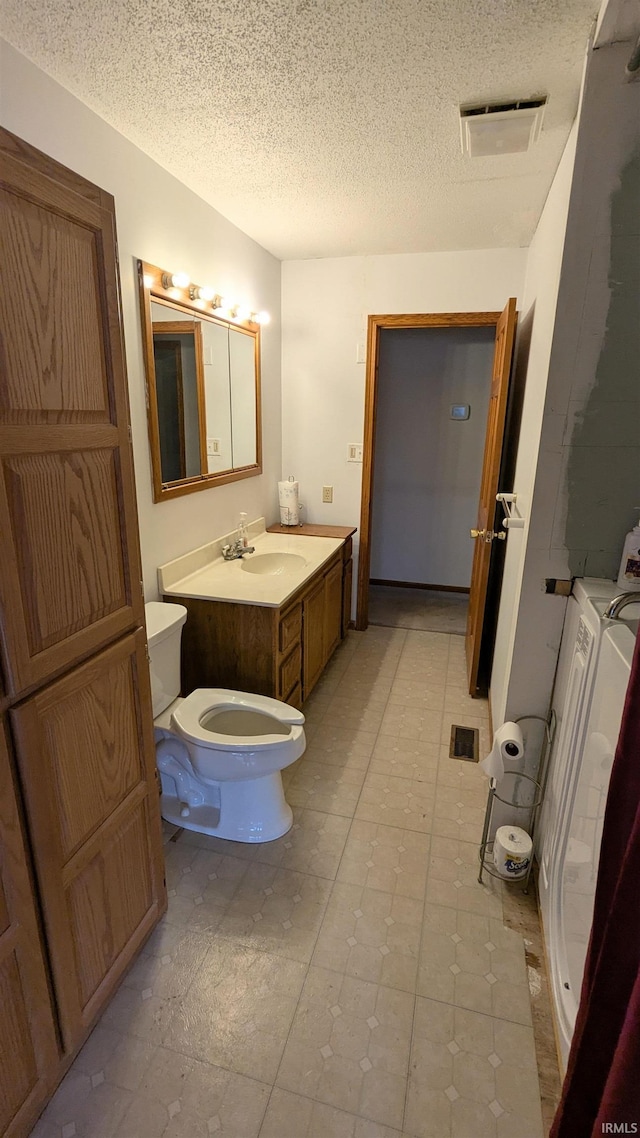 bathroom featuring visible vents, toilet, vanity, a textured ceiling, and washer and dryer