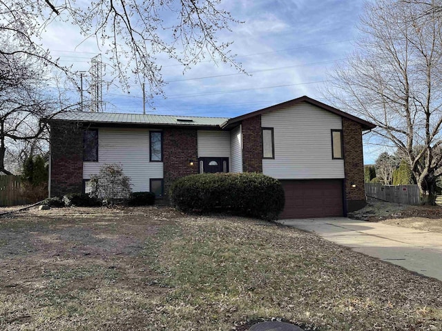 raised ranch featuring an attached garage, fence, metal roof, and concrete driveway