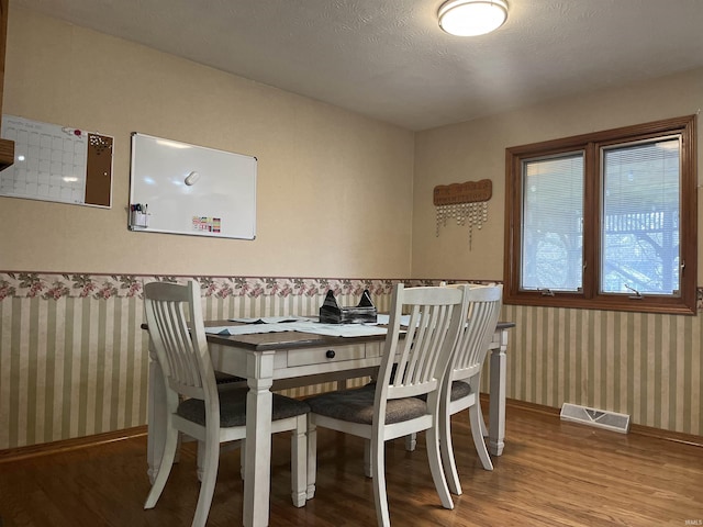 dining space featuring visible vents, a textured ceiling, wood finished floors, baseboards, and wallpapered walls