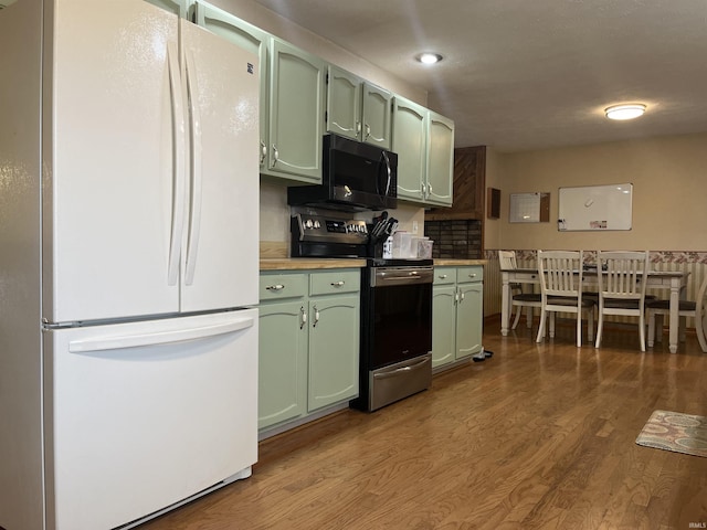 kitchen with wood finished floors, green cabinets, light countertops, freestanding refrigerator, and stainless steel electric range oven