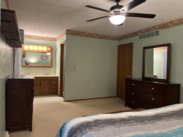 bedroom with a textured ceiling, light carpet, a sink, visible vents, and ensuite bath