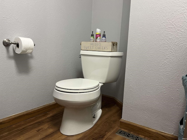 bathroom with toilet, baseboards, wood finished floors, and a textured wall