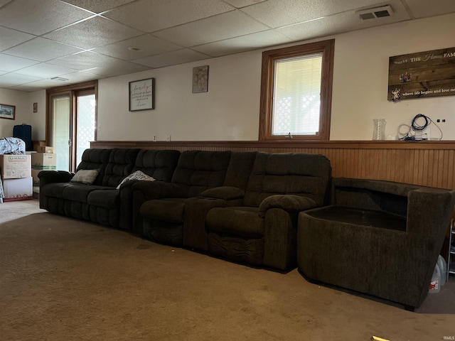 carpeted living area with a paneled ceiling, wainscoting, and visible vents